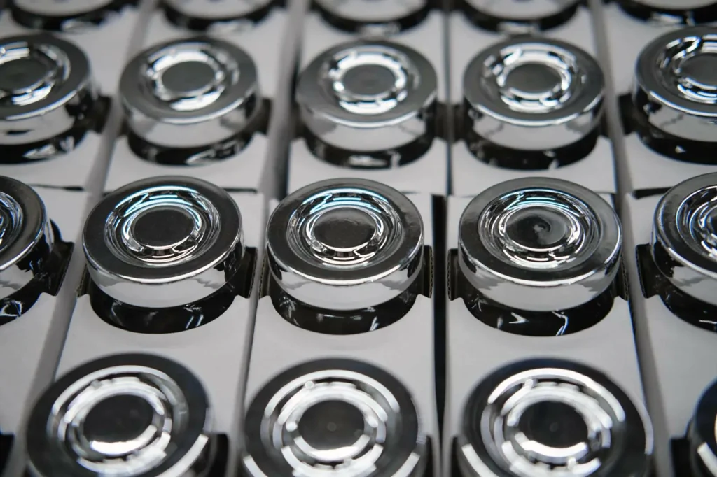 Tappi metallici cromati e lucidi disposti in fila su una linea di produzione, che mostrano la finitura liscia e riflettente ottenuta con l'elettrolucidatura per imballaggi di alta qualità.