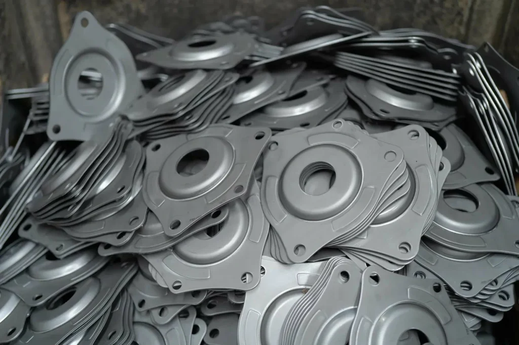 Une pile de pièces métalliques estampées attend d'être affinée par des services de finition des surfaces métalliques.