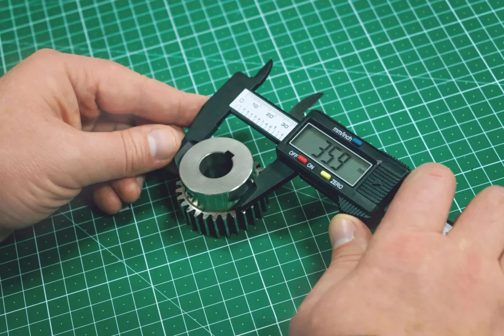 Technician measuring a precision-machined gear with digital calipers, verifying dimensional accuracy post-grinding or milling.