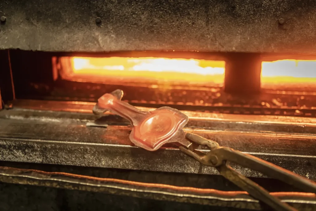 Pièce métallique chauffée au rouge et manipulée avec des pinces lors d'un traitement thermique dans un four industriel.
