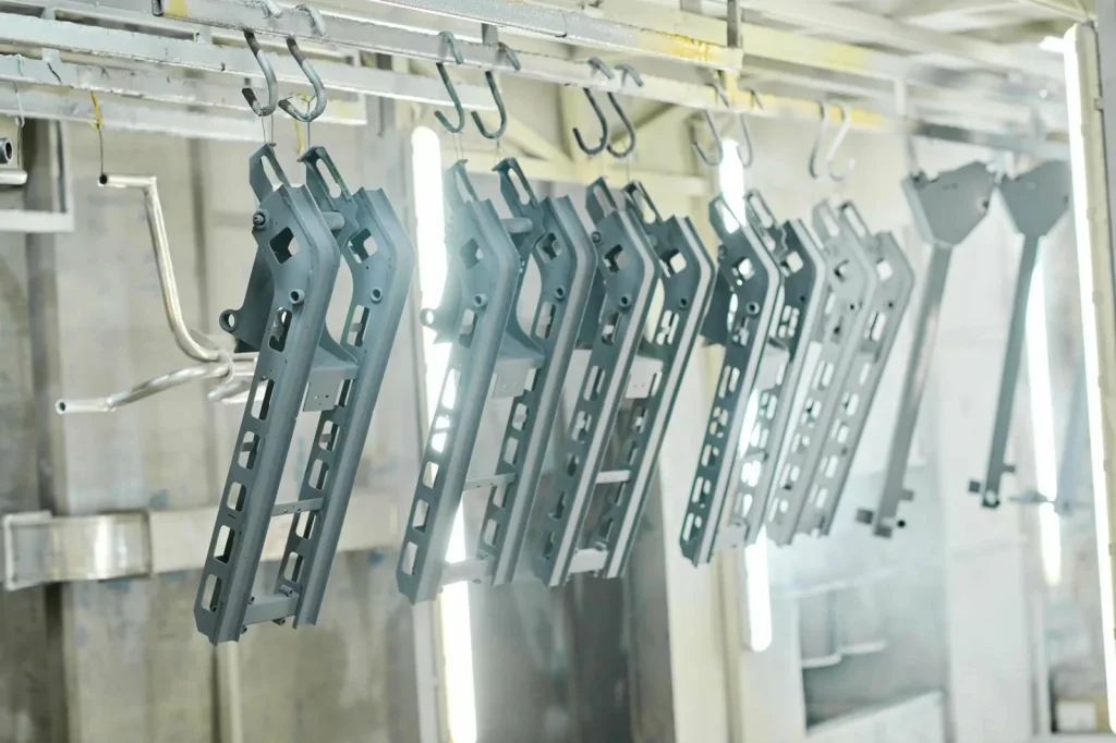 Staffe metalliche grigie appese a un nastro trasportatore in una fabbrica, la cui finitura superficiale uniforme evidenzia la precisione dell'elettrolucidatura per i componenti industriali.