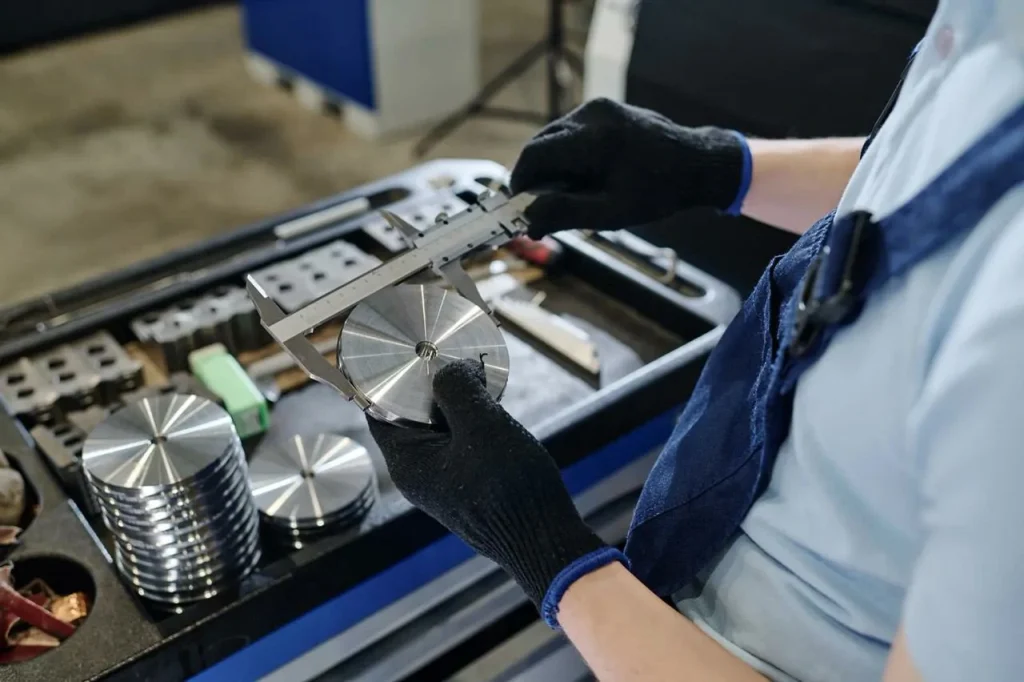 Technik měří přesný kovový kotouč pomocí kaliperů, aby ověřil přesnost rozměrů po tvrdém frézování.