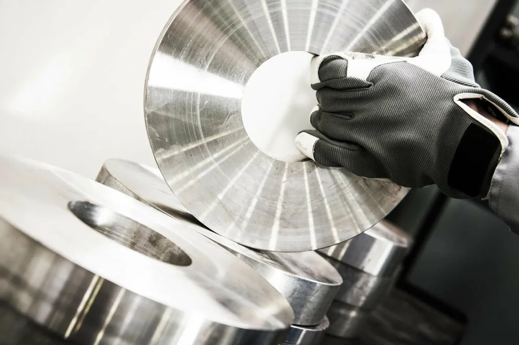Une main gantée manipule un disque métallique brillant, produit fini des services de finition des surfaces métalliques.