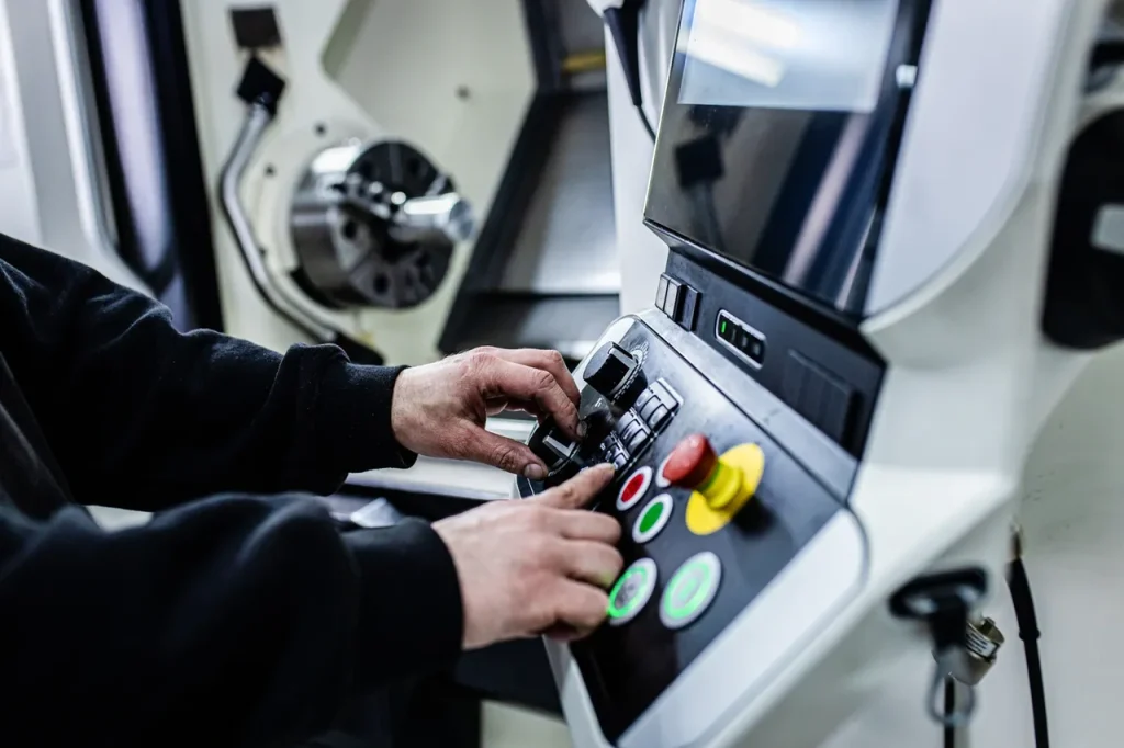 Operario ajustando los controles del torno CNC, demostrando el contraste de complejidad de programación entre el mecanizado CNC y el moldeo por inyección.