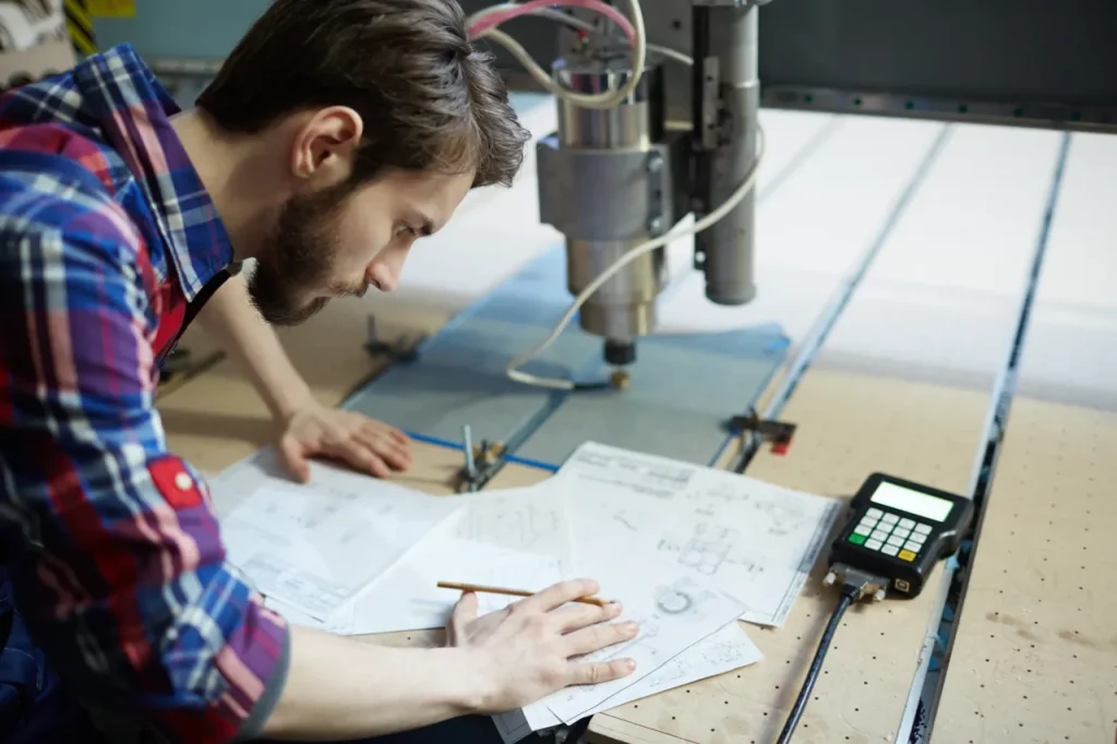 Ingeniero revisando dibujos técnicos en una máquina CNC, comparando los flujos de trabajo de diseño entre el moldeo por inyección y el mecanizado CNC.