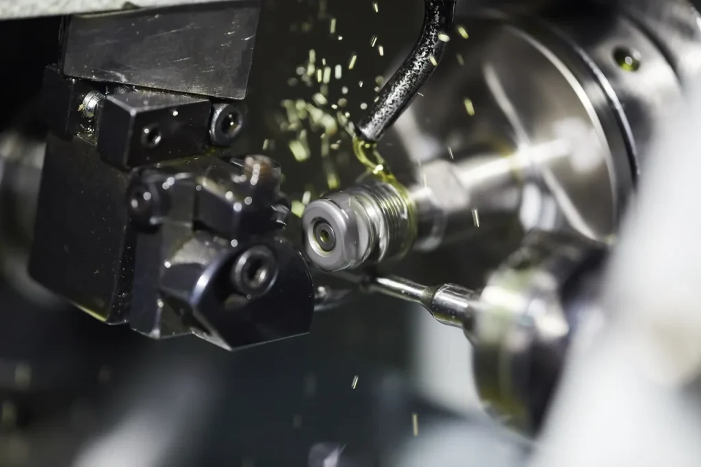 Operación de torneado CNC con lubricación, utilizando refrigerante para reducir la fricción y evitar el gripado del metal en componentes roscados.
