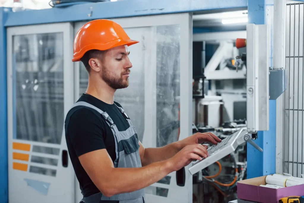 Operario de fábrica programando una máquina CNC, aplicando controles de proceso para evitar el gripado del metal durante el mecanizado de precisión.