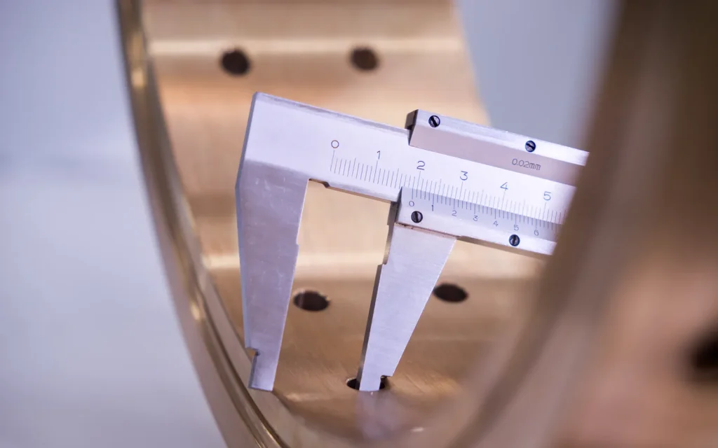 Precision caliper measuring a machined metal aerospace component with tight tolerances.