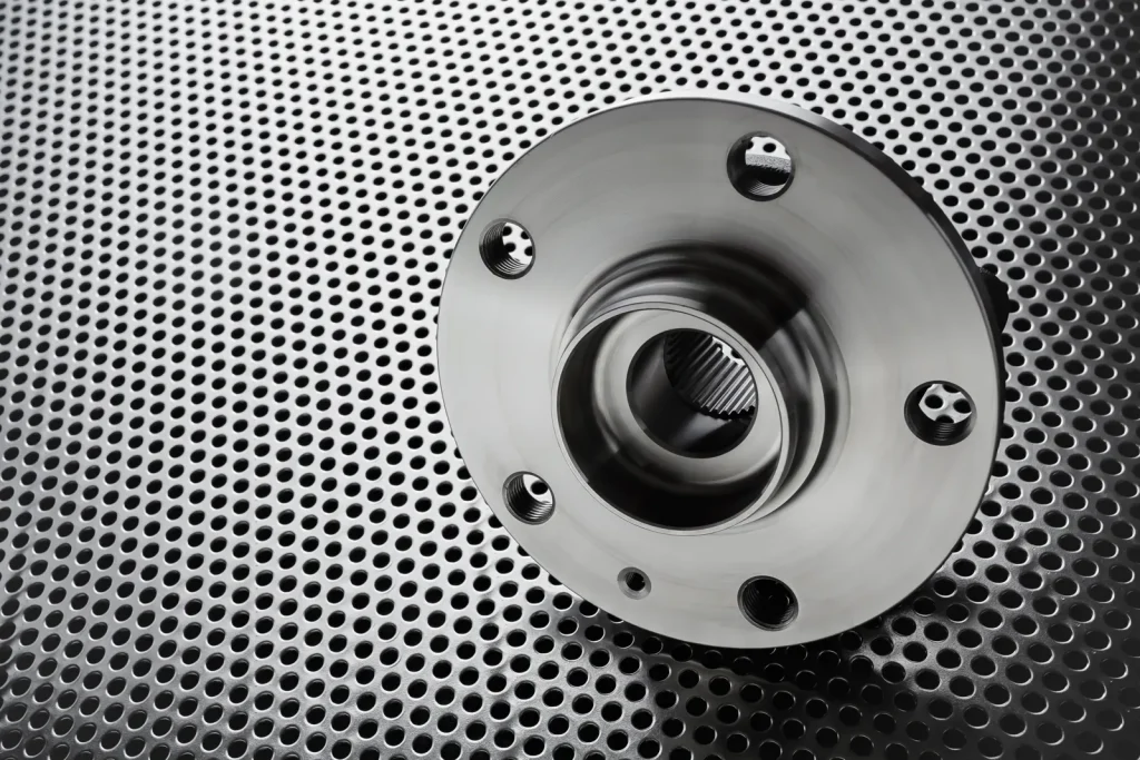 Finished precision-machined metal wheel hub component on a perforated metal background.