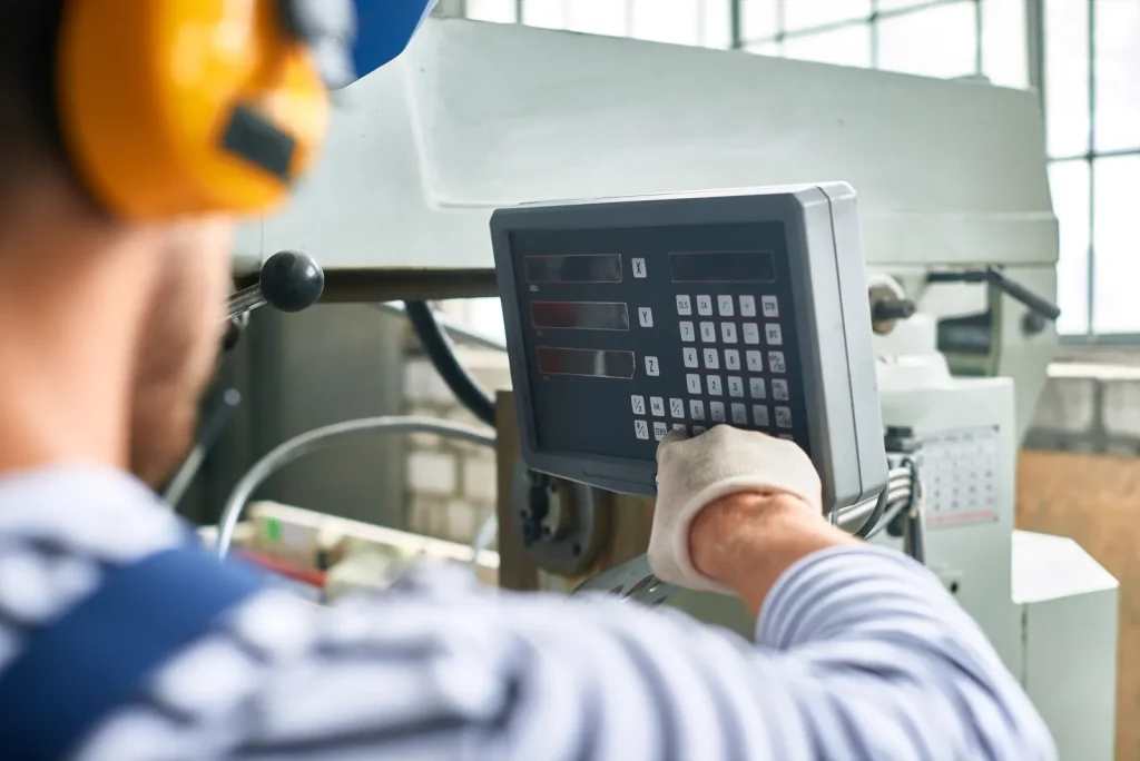 Factory worker operating a CNC machine control panel in a manufacturing setting.