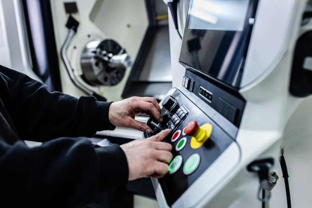 Operatore che regola il pannello di controllo di una macchina CNC, con l'attenzione alle mani che interagiscono con pulsanti e manopole.