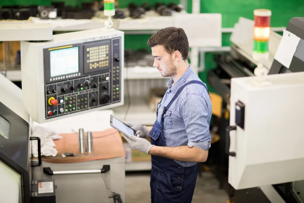Zerspanungsmechaniker, der eine CNC-Maschine mit einem Tablet bedient und Parameter für die Bearbeitung von Titan- und Wolframwerkstoffen programmiert.