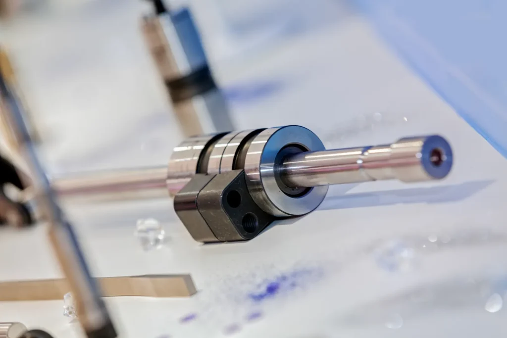 Finished high-precision metallic mechanical shaft component with polished surface displayed on white workbench after CNC machining production.
