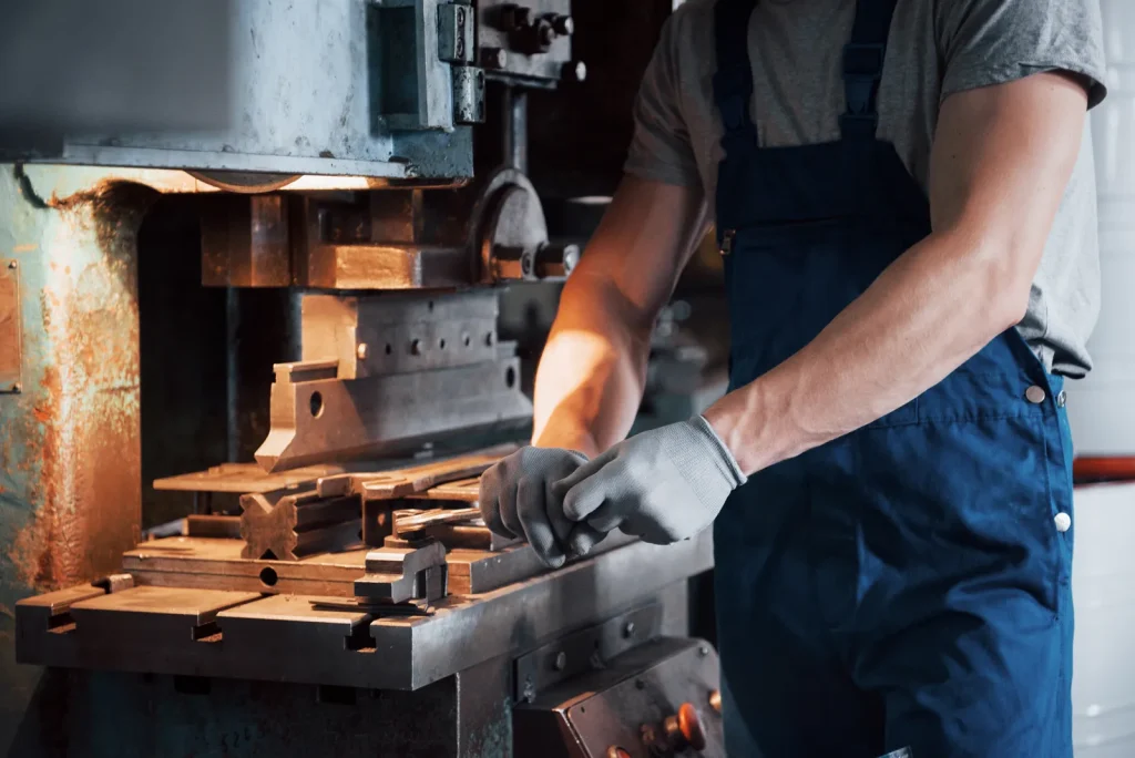Un ouvrier d'usine, équipé de gants de protection, règle une matrice d'estampage métallique sur une presse industrielle afin de fabriquer des pièces métalliques estampées sur mesure.