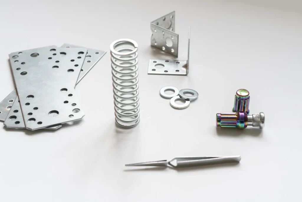 Assortiment de pièces métalliques embouties sur mesure, comprenant des tôles perforées, des ressorts, des cornières et des pièces de quincaillerie de précision, sur fond blanc uni.