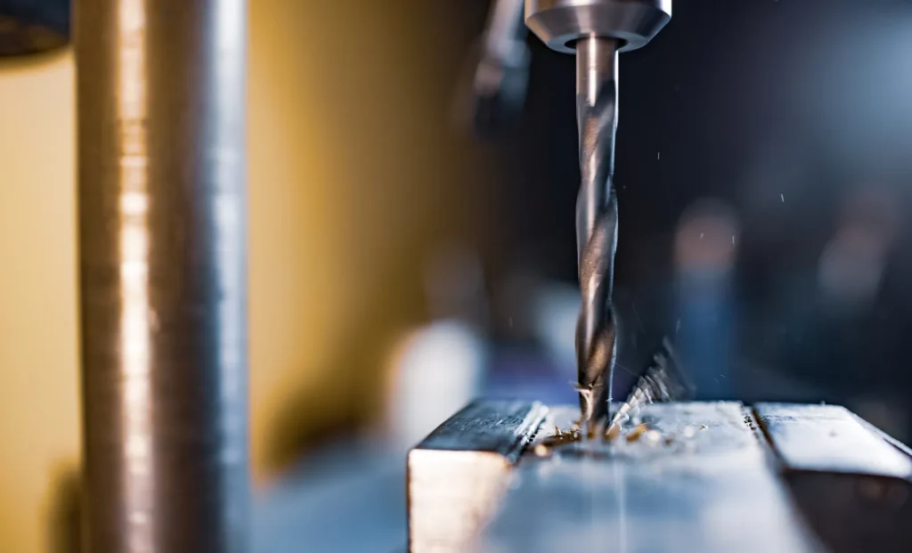 Gros plan sur un foret métallique en rotation servant à percer des trous dans une pièce métallique pleine, générant des copeaux de métal lors d'une opération d'usinage CNC de précision.