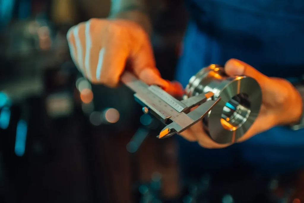 Un opérateur utilise un pied à coulisse manuel pour mesurer les dimensions d'une pièce métallique polie et finie, dans le cadre d'un contrôle qualité après un usinage CNC.