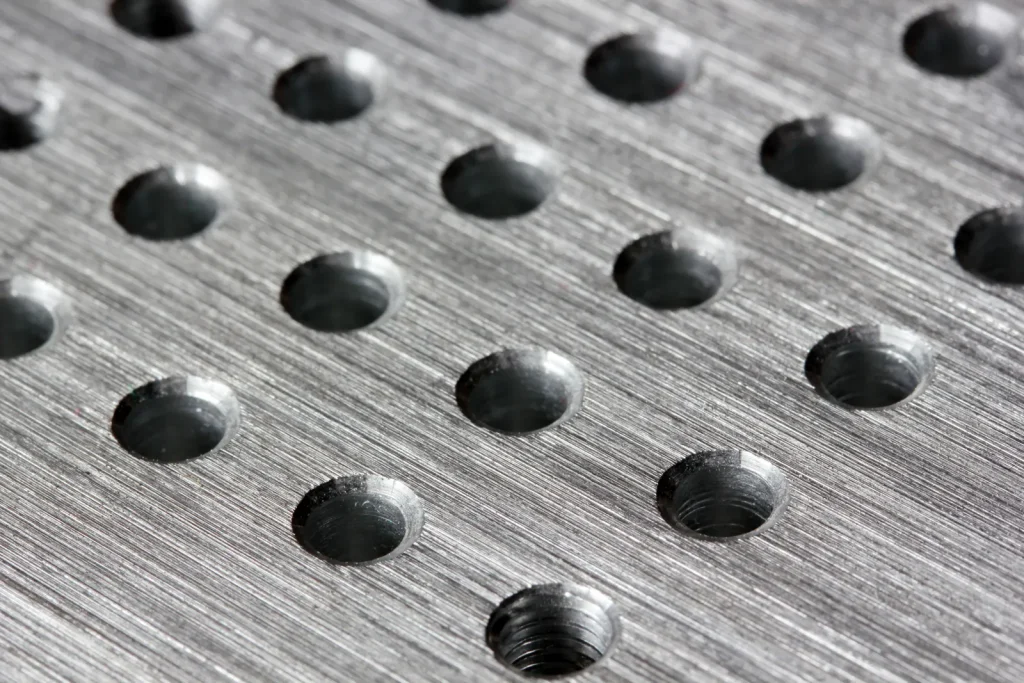 Gros plan sur une plaque d'aluminium présentant des trous filetés soigneusement usinés, illustrant la précision des perçages obtenus grâce aux procédés d'usinage CNC des métaux.