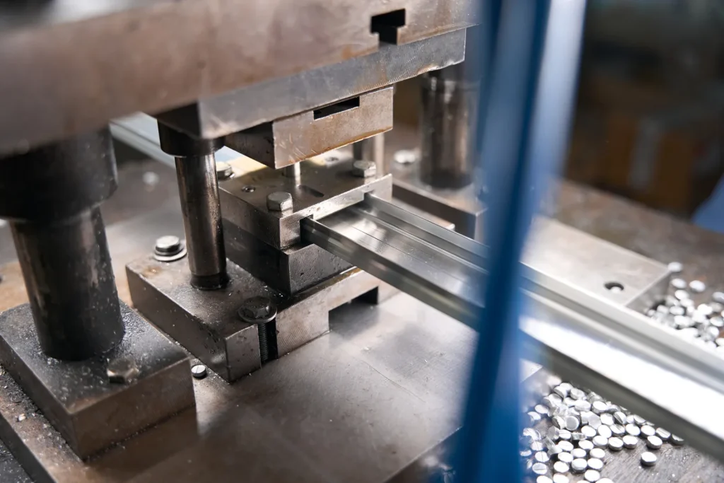 Ensemble de matrices pour presse à estamper industrielle, alimenté par une bande métallique plate qui passe à travers l'outil de formage, tandis que des chutes métalliques s'accumulent à côté du socle de la machine.