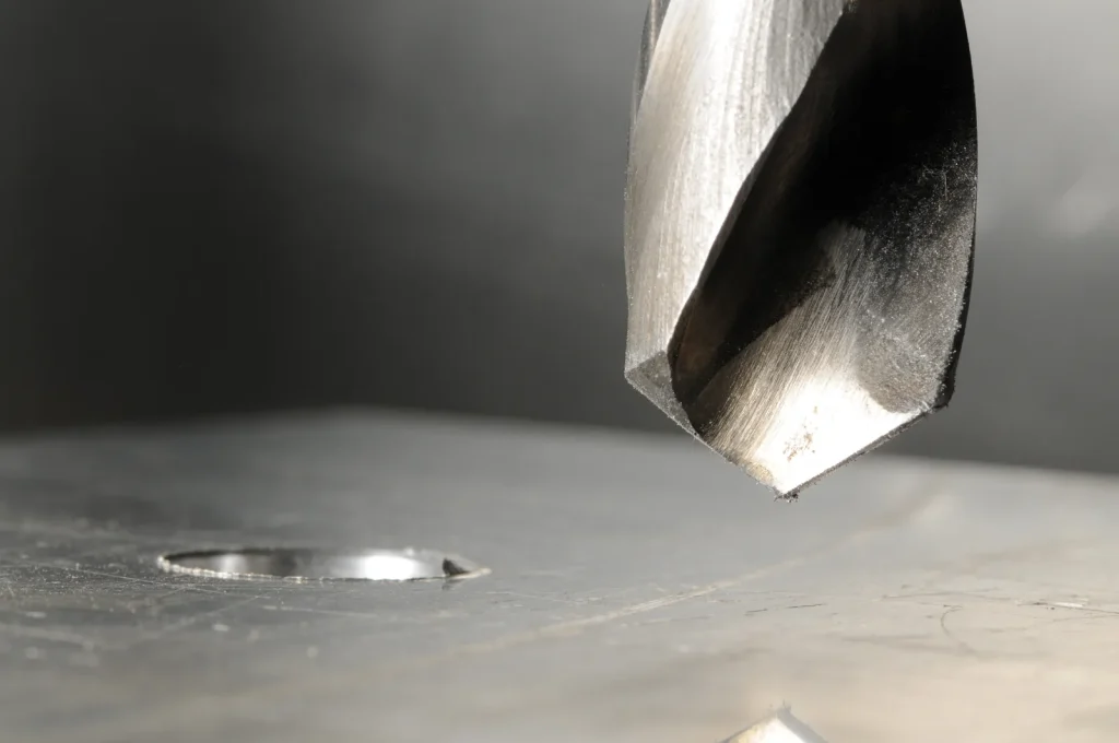 A drill bit prepares to perform EDM hole drilling on a metal plate.