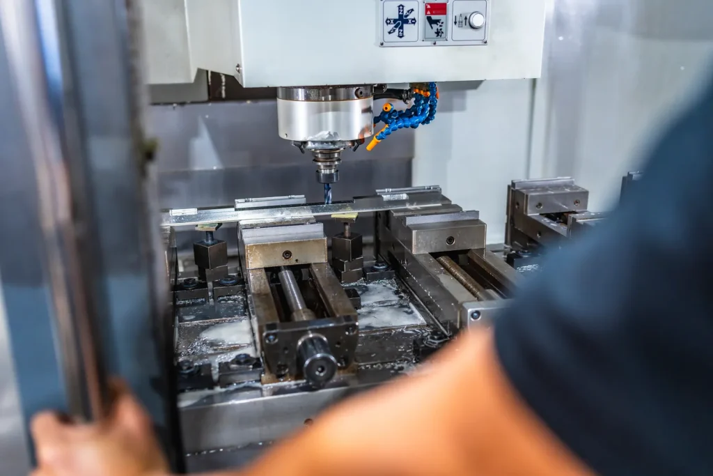 Operatore che osserva una macchina CNC mentre esegue il taglio di un pezzo metallico con liquido di raffreddamento
