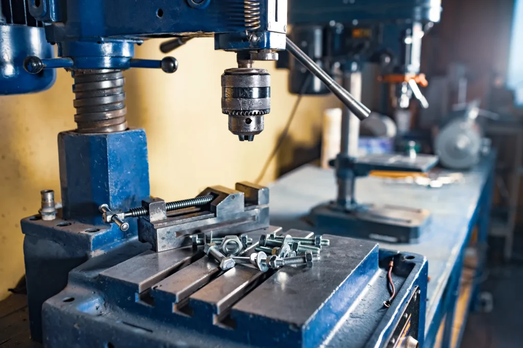 A drill press prepares parts for custom metal stamping services in a workshop.