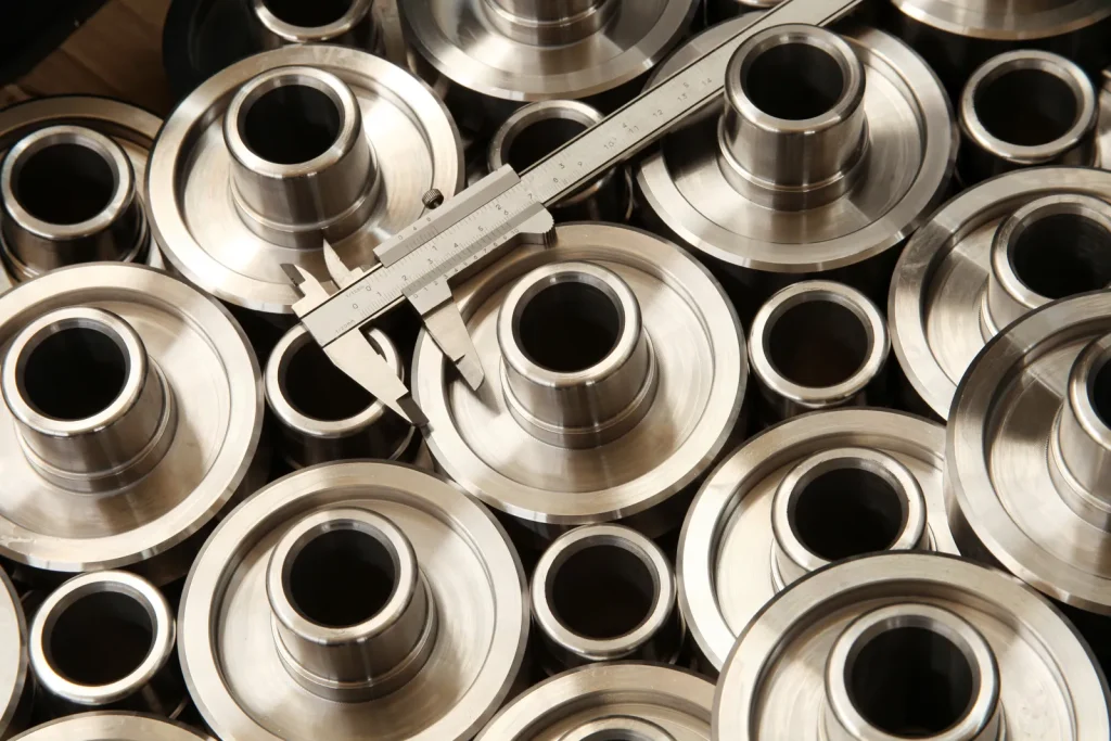 A caliper measures a batch of finished titanium parts made via CNC turning.