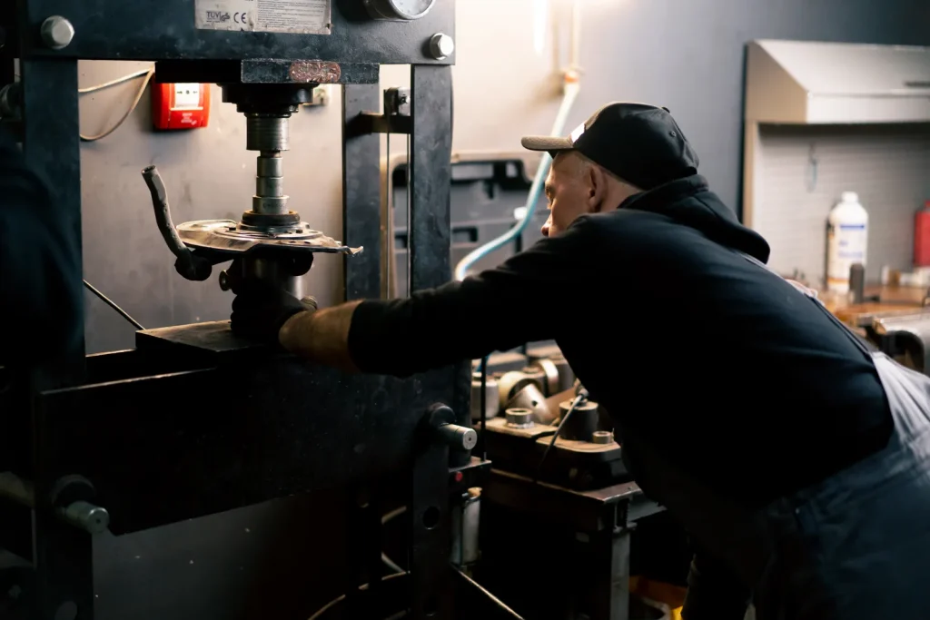 Pracownik fabryki obsługuje przemysłową hydrauliczną prasę tłoczącą w celu uformowania metalowego elementu piasty samochodowej przy użyciu matrycy transferowej w warsztacie.